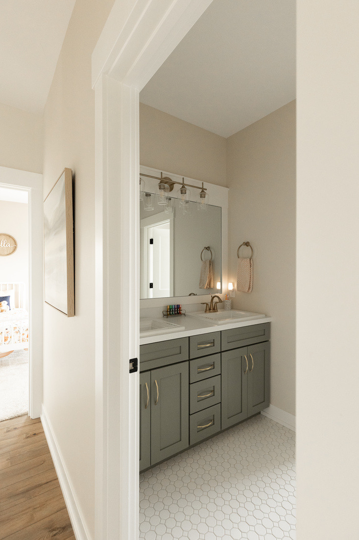Double vanity bathroom with sage green cabinets and white hex tile flooring in West Michigan remodel by Ridgewood Home Construction