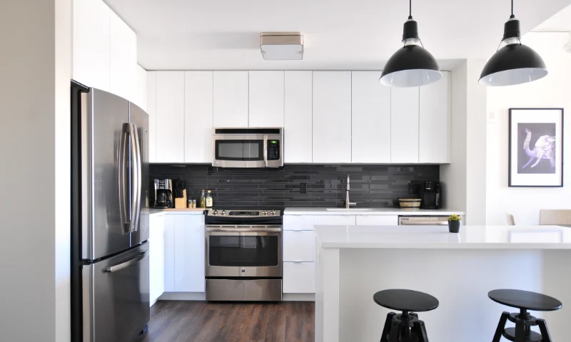 A modern kitchen refresh in West Michigan, with stainless steel appliances, white cabinets, a black tile backsplash, and two black pendant lights above a white island with two black stools.