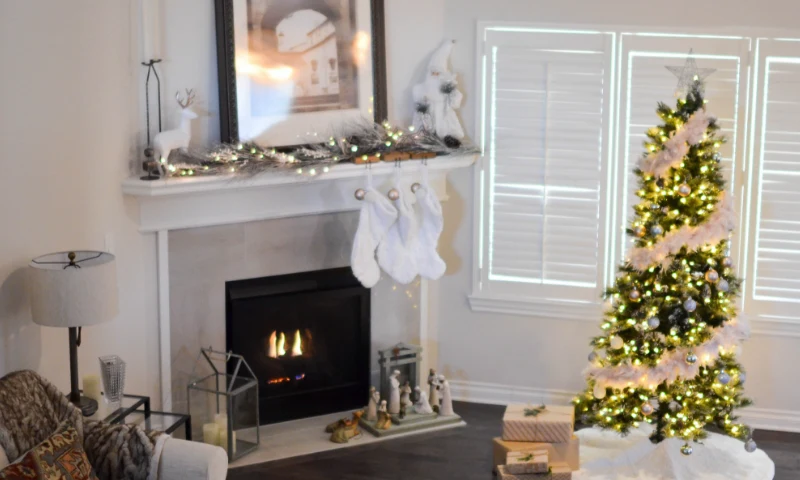 A living room refreshed for Christmas in Grand Rapids, MI, with a lit fireplace, stockings on the mantel, a Christmas tree with lights, and wrapped gifts on the floor.