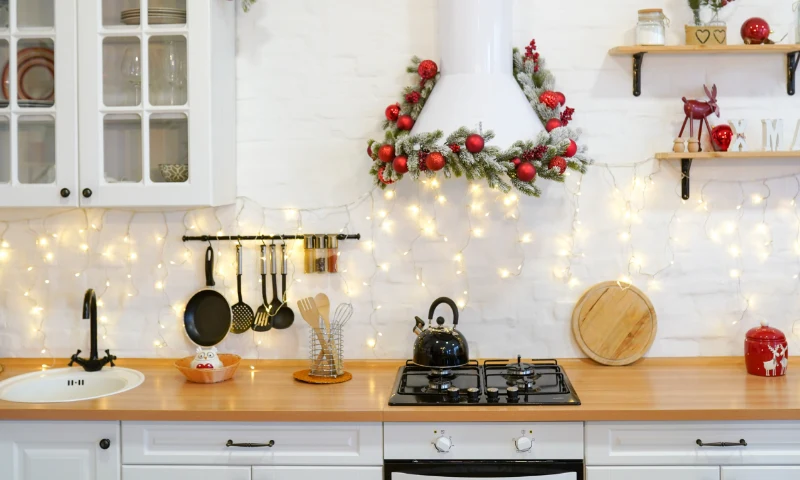 A kitchen refresh in Grand Rapids, MI, for the holidays with string lights, red ornaments, and a festive wreath on the stove hood; cookware and utensils are neatly displayed on the countertop and shelves.