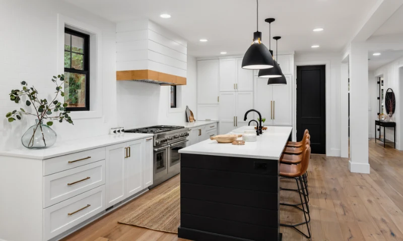 A modern kitchen in Grand Rapids, Michigan, with white cabinets, stainless steel appliances, a black island, brown leather stools, pendant lights, and wood flooring offers a refreshing update to any home.
