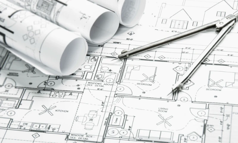 Architectural blueprints with detailed floor plans are spread out, accompanied by rolled-up drawings and a metal compass for drafting—a perfect scene to refresh design ideas.