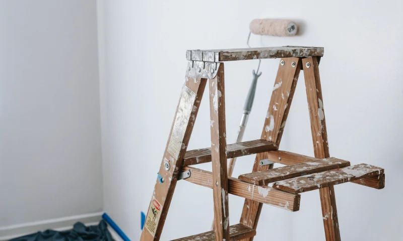 A paint-splattered wooden ladder stands in front of a white wall with a paint roller resting on it, hinting at a refreshing update in progress.