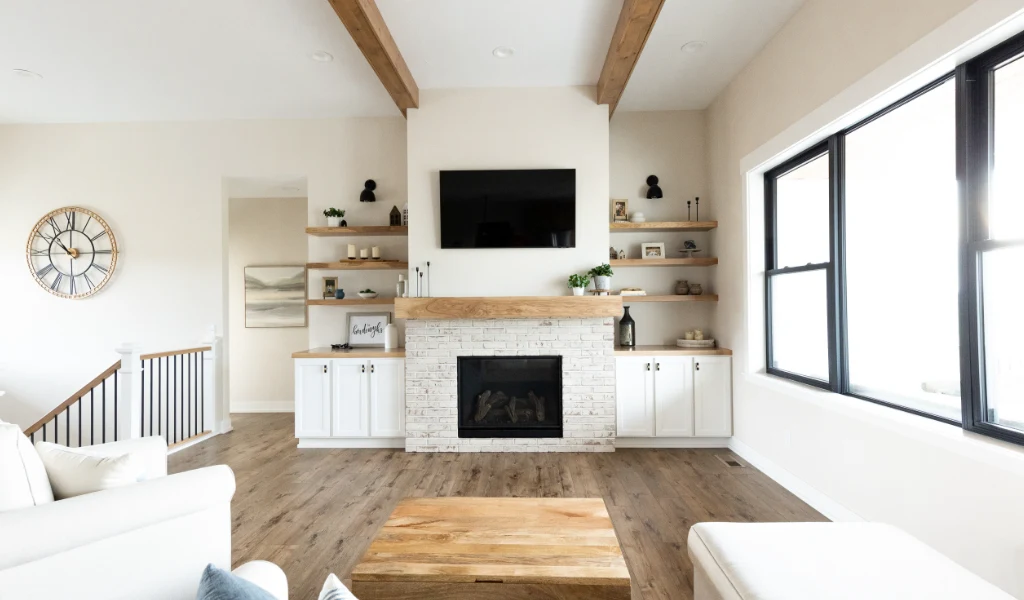 Modern Allendale Main Floor living room with a wall-mounted TV above a fireplace, built-in shelves, large windows, wood flooring, and neutral-toned furniture.