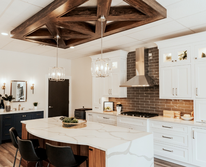 Modern kitchen with white cabinets, a marble island, stainless steel appliances, and brown subway tile backsplash—this stunning space highlights every detail of the remodeling process, from the pendant lights to the wood ceiling feature.