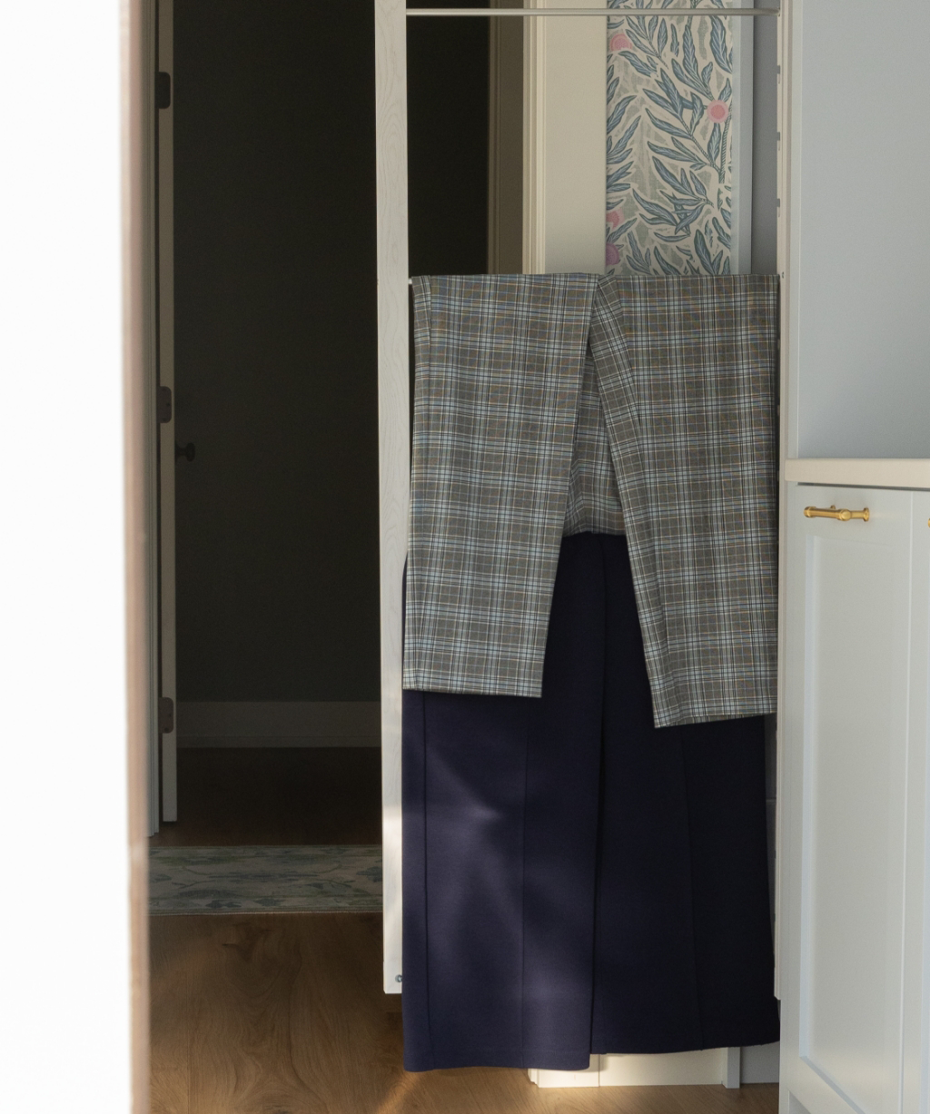 A pair of checkered pants and navy trousers hang neatly over a white door in a brightly lit room, showcasing the organized style resulting from a Byron Center Whole Home Remodel.