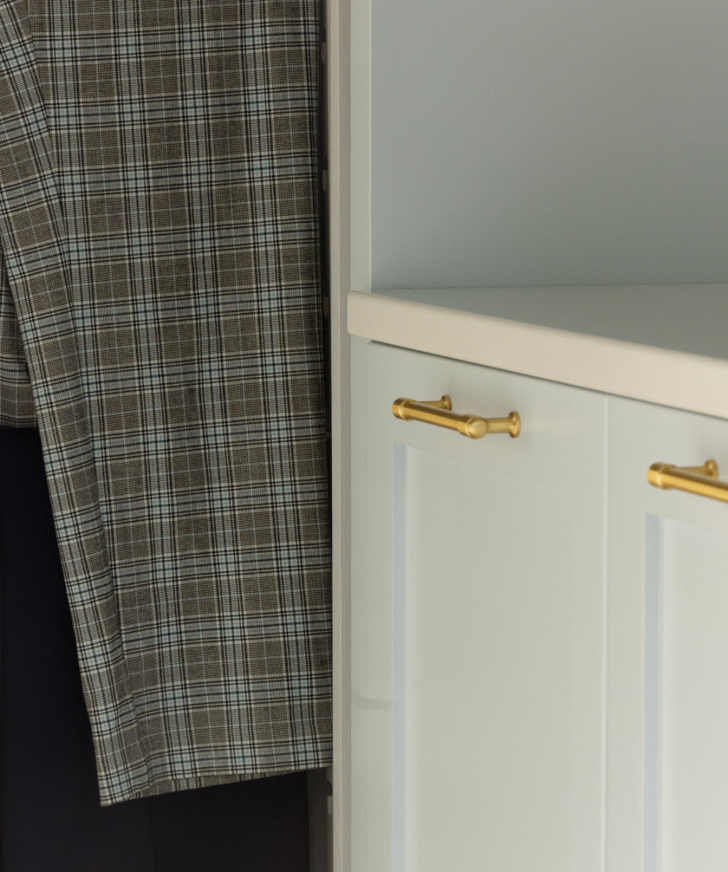 A plaid jacket hangs next to a white cabinet with gold handles, a detail from a recent Byron Center Whole Home Remodel.