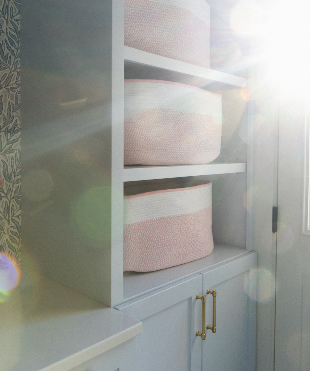 Two pink and white woven baskets on white shelves, with sunlight streaming in from the right and creating lens flares—a charming detail from a recent Byron Center Whole Home Remodel.