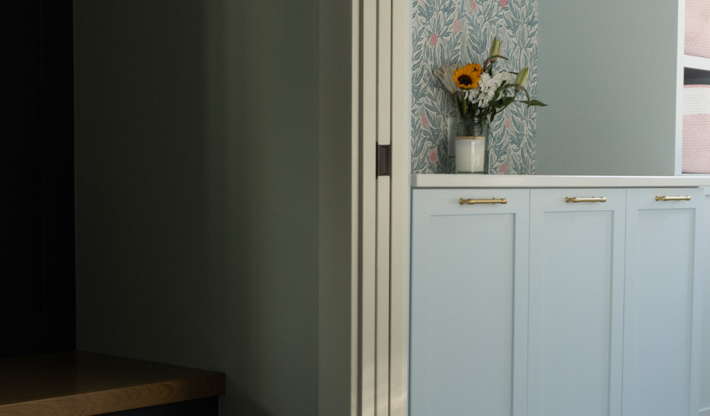 A vase with flowers sits on a light blue cabinet next to a wall with patterned wallpaper and a vertical white radiator, showcasing the elegance of a Byron Center Whole Home Remodel.