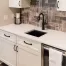 A modern kitchen remodel in Sparta, MI, with white cabinets, black handles, a black faucet, tile backsplash in a herringbone pattern, and a white countertop—perfect inspiration if you want to plan a home addition or upgrade your current space.