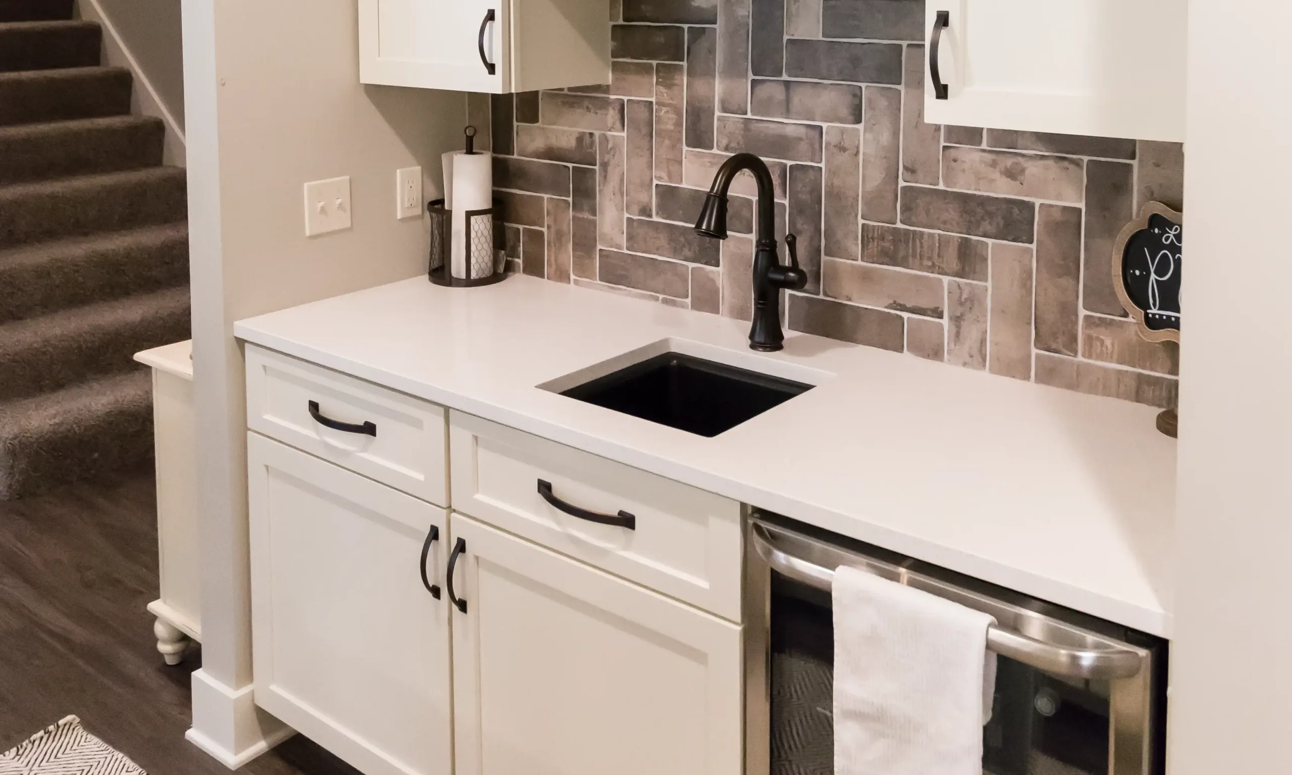 A modern kitchen remodel in Sparta, MI, with white cabinets, black handles, a black faucet, tile backsplash in a herringbone pattern, and a white countertop—perfect inspiration if you want to plan a home addition or upgrade your current space.